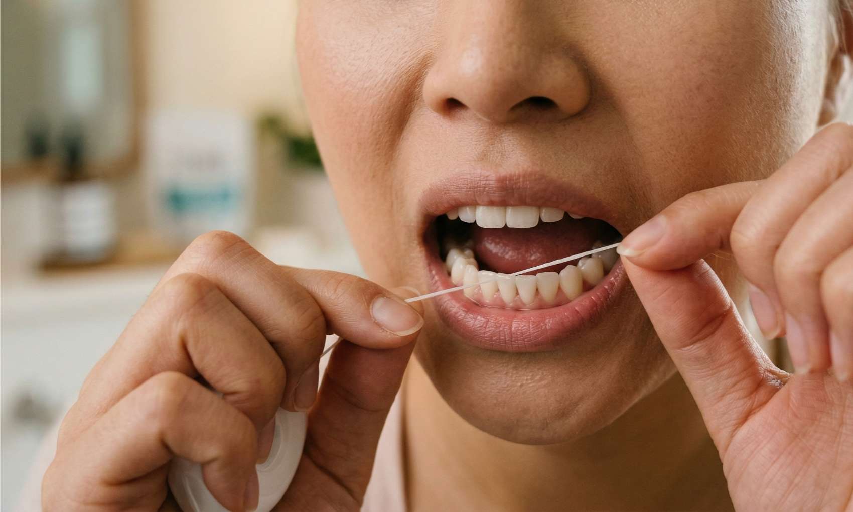 치아 사이 충치 예방을 위해 양손으로 치실을 팽팽하게 잡고 앞니 사이를 관리하는 여성의 입 주변 클로즈업