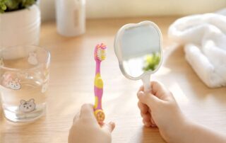 밝은 테이블 위에서 어린이 칫솔과 작은 거울을 쥐고 있는 아이의 작은 손