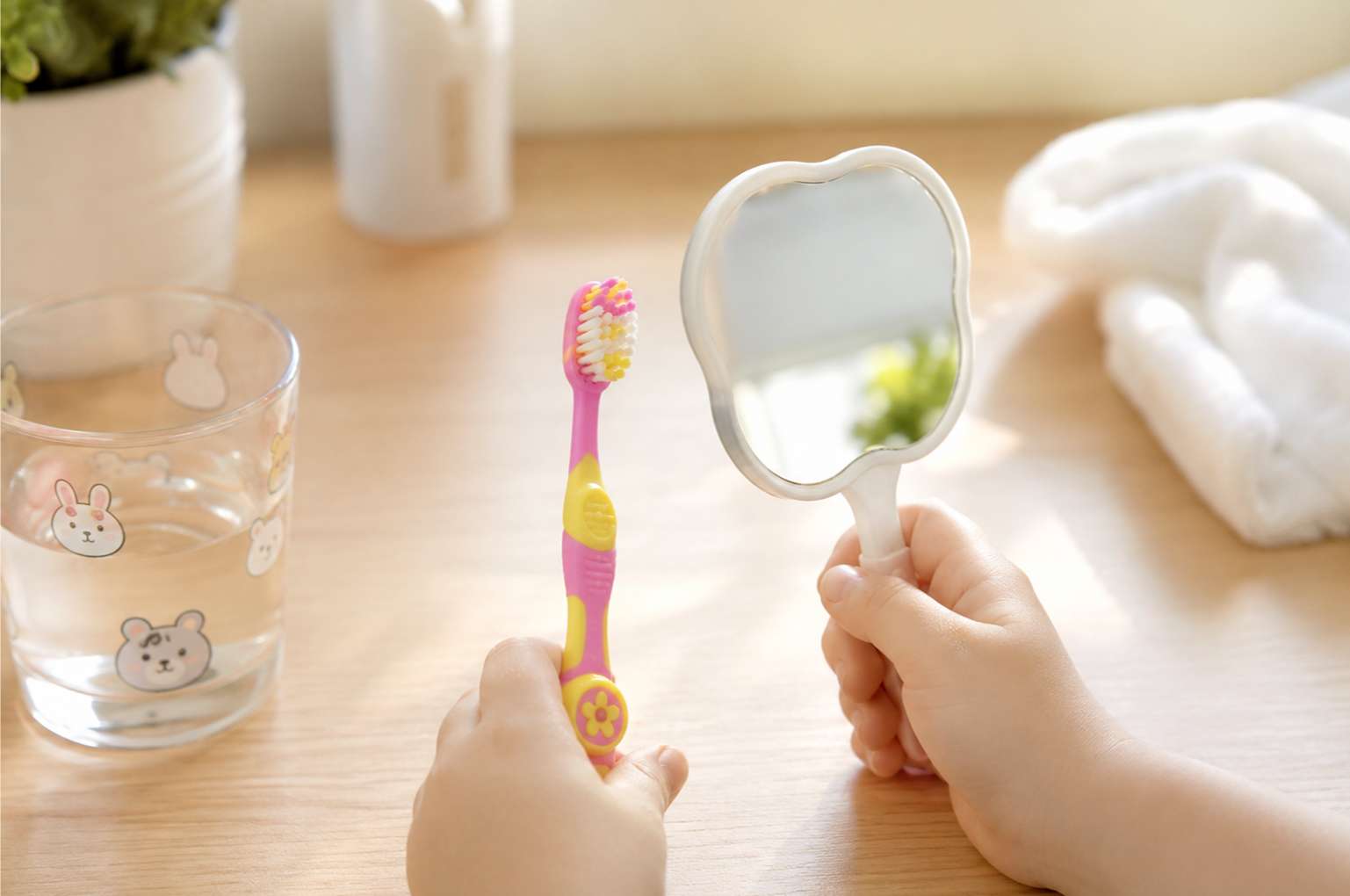 밝은 테이블 위에서 어린이 칫솔과 작은 거울을 쥐고 있는 아이의 작은 손